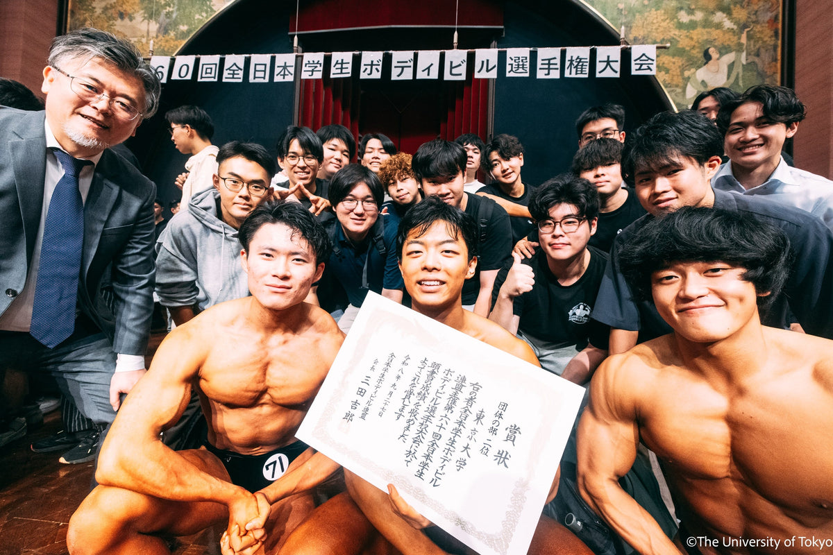 第60回全日本学生ボディビル選手権大会の横断幕の前で、団体準優勝の賞状を手に喜ぶ東京大学B&W部の部員たち